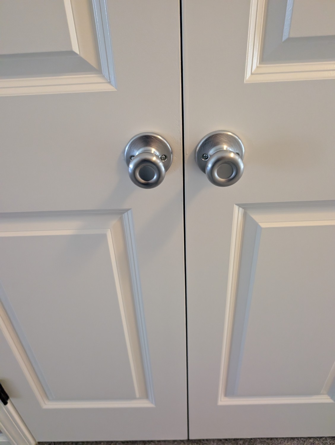 Matching silver knobs installed on a pair of white closet doors.