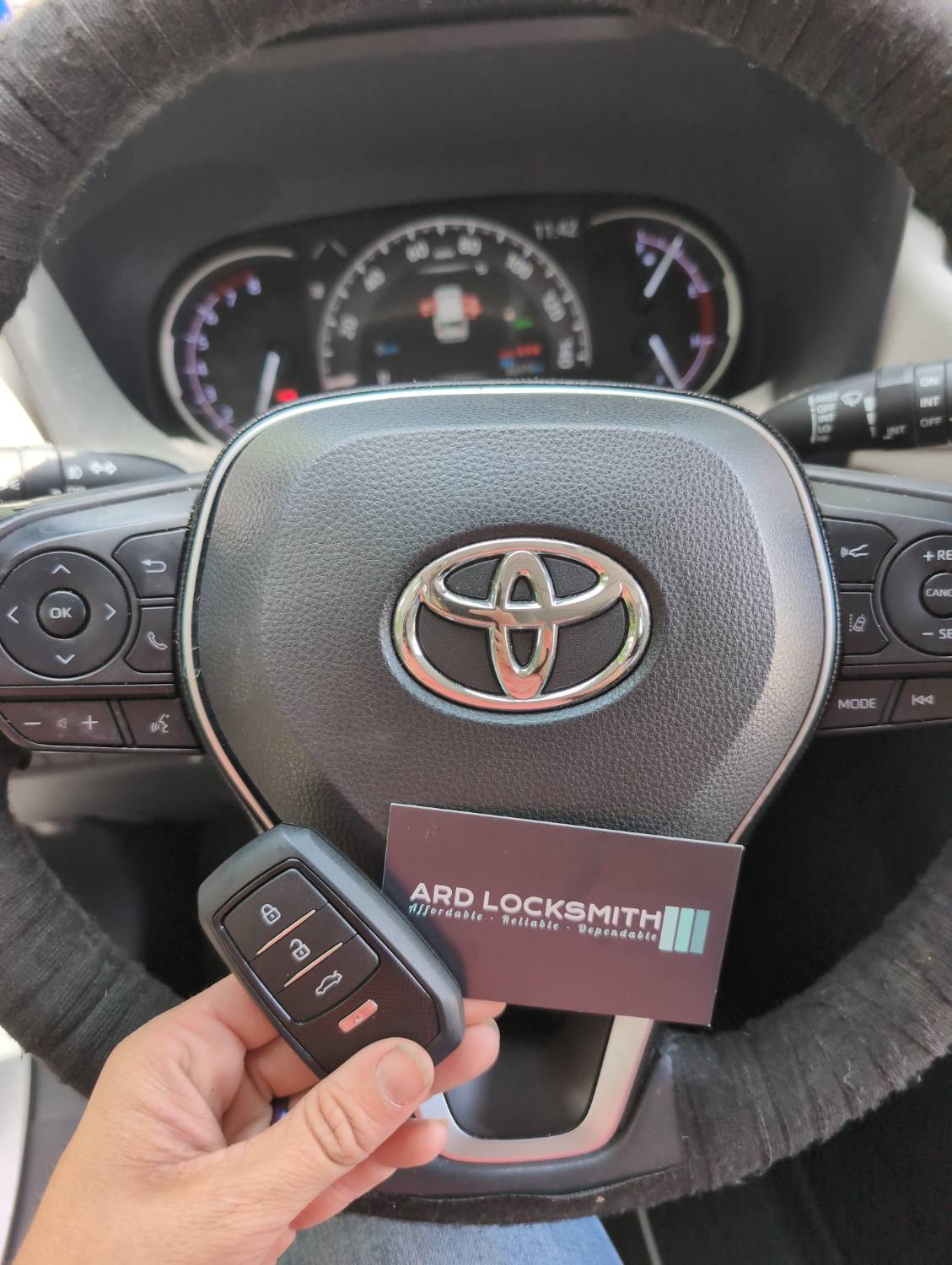 Toyota smart key fob held beside an ARD Locksmith card inside a Toyota RAV4.